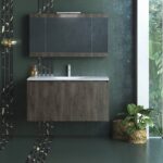 Modern bathroom vanity with dark wood cabinets, a white countertop sink, and a green textured wall, plus a bottle on the counter.