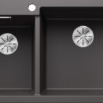 Double kitchen sink in dark gray with two basins and stainless steel drain strainers.