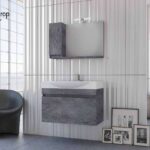 Modern bathroom with a floating grey stone vanity, matching wall cabinet, and a curved gray chair beside framed art on the floor along a vertical-panel wall.
