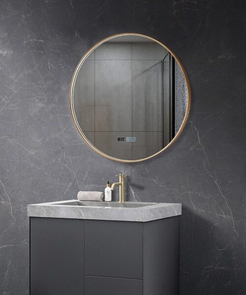 Round gold-framed mirror above a dark gray bathroom vanity with a marble countertop and brass faucet, on a dark marble wall