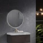 Round backlit mirror above a wall-mounted vanity with gray marble top and a gold faucet in a dark marble bathroom surface style