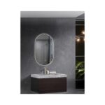 Contemporary bathroom with dark marble walls, an oval backlit mirror, and a marble-topped vanity with a gold faucet; shelving and warm lights visible to the right.