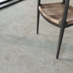 Close-up of a dark wooden chair with a tan woven seat resting on light gray stone tile flooring