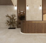 Modern foyer with curved wooden reception desk, beige stone walls, and a sculptural driftwood centerpiece on the left.