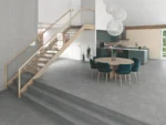 Open-plan kitchen and dining area with a wooden staircase, teal cabinets, a round dining table with teal chairs, and three white globe pendant lights.
