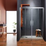 Modern glass shower enclosure with metal frame in a dark-toned bathroom, a wooden stool with a towel inside view, and a sink on the left.