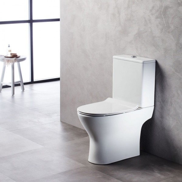 Modern white toilet against a textured gray wall in a bright, minimalist bathroom with large window in the background and a small table nearby.