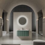 Modern bathroom with a circular backlit mirror above a green floating vanity centered on a gray wall.