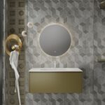 Modern bathroom with geometric gray tiles, a round backlit mirror, and a gold floating vanity under a white sink.